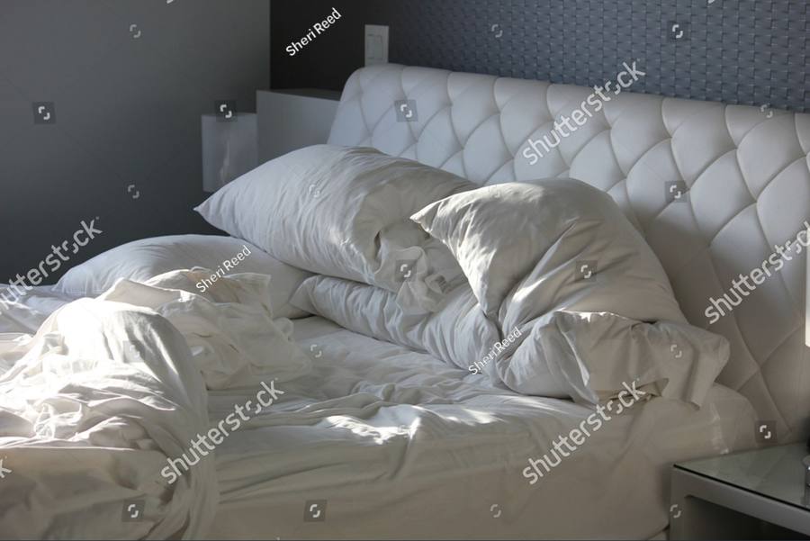An unmade bed in dim morning light