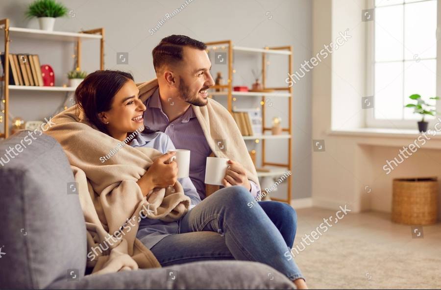 A couple sitting together under a blanket with mugs of tea