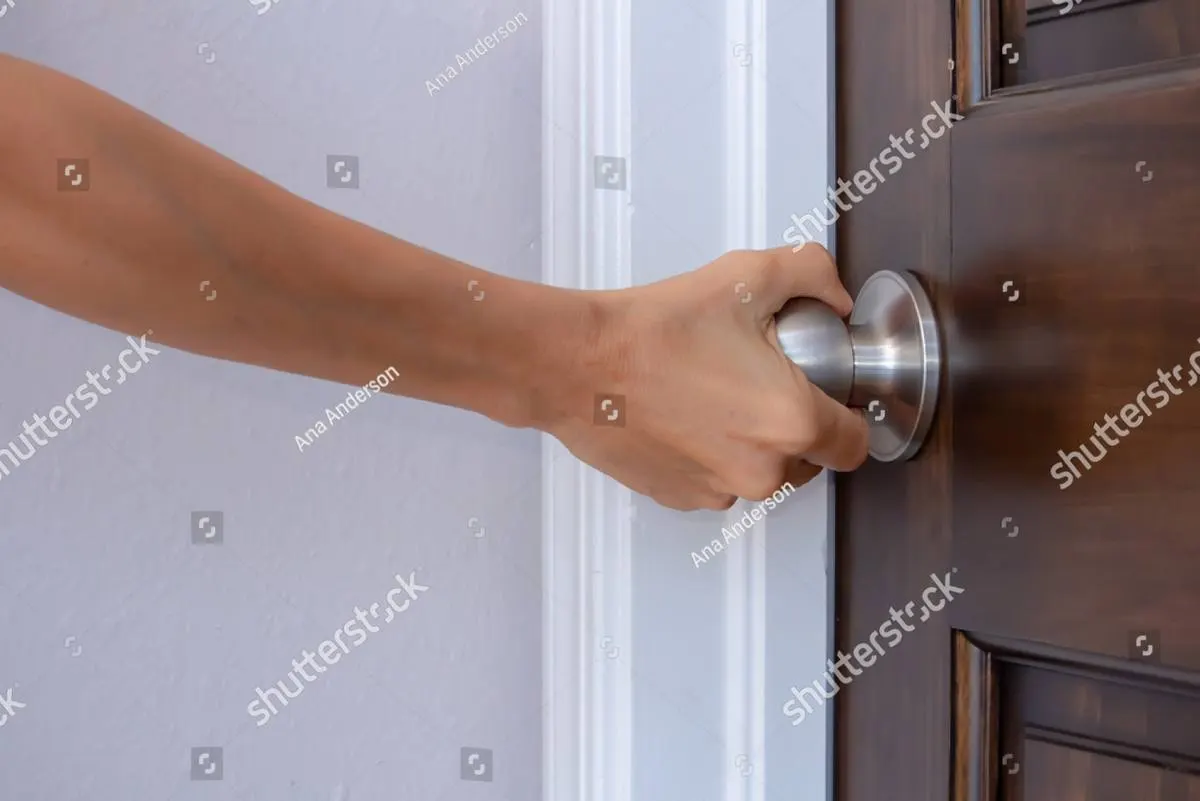 A hand closing on a doorknob beside a white wall