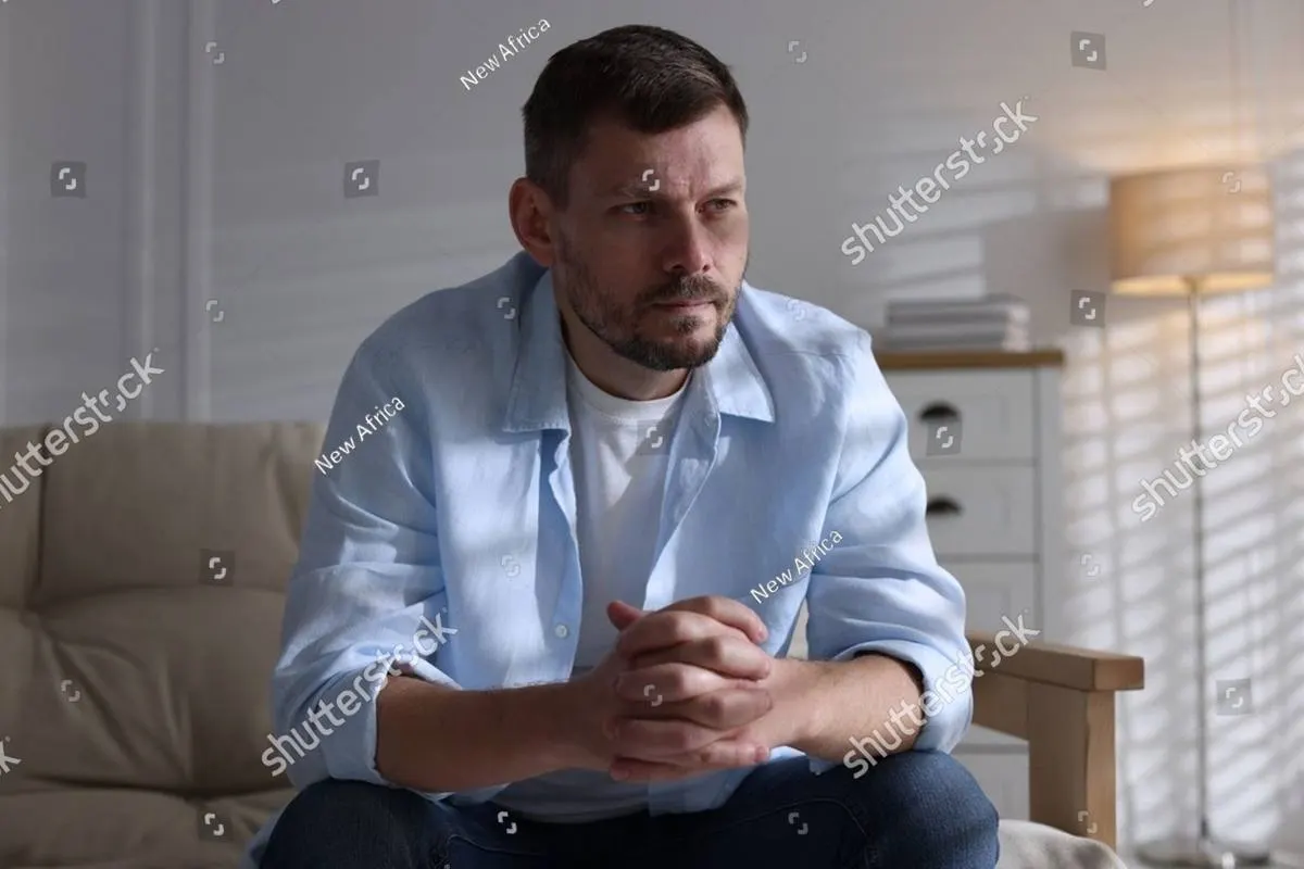 A man sitting on a sofa with his hands clasped, looking away