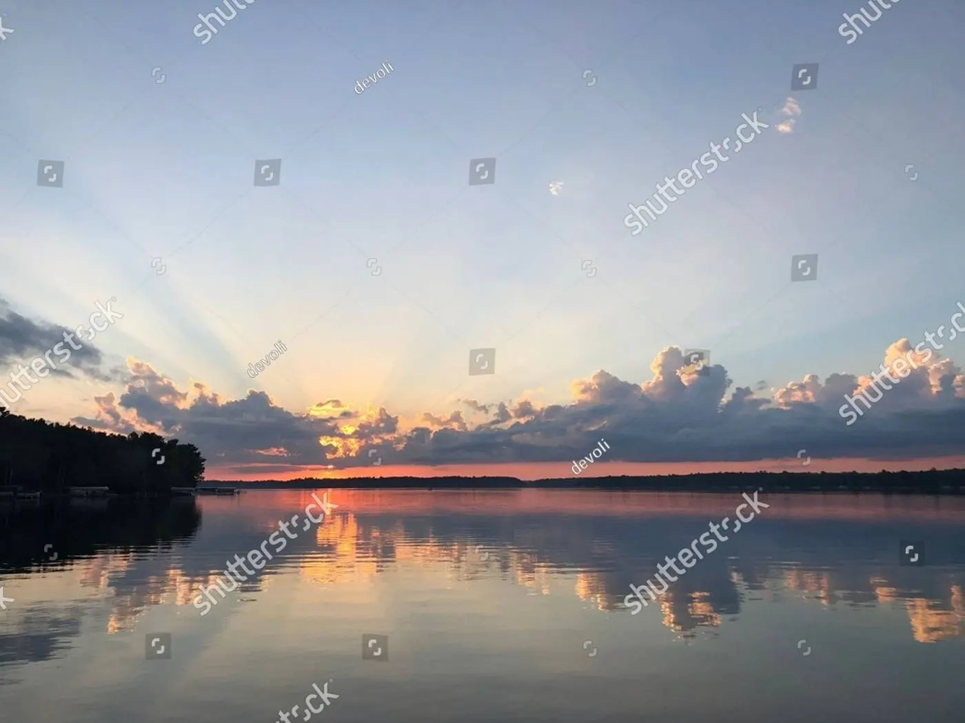 Sunrise over a lake, rays fanning up through a low cloud bank